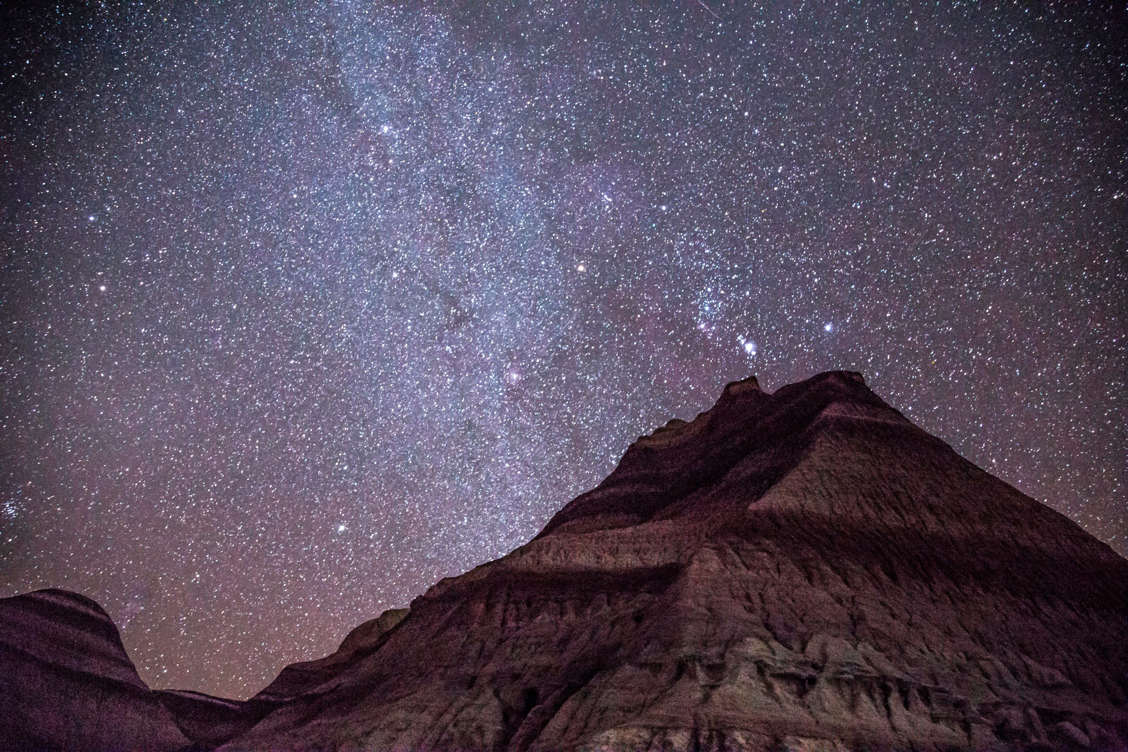 Dark blue sky filled with stars over banded badland.